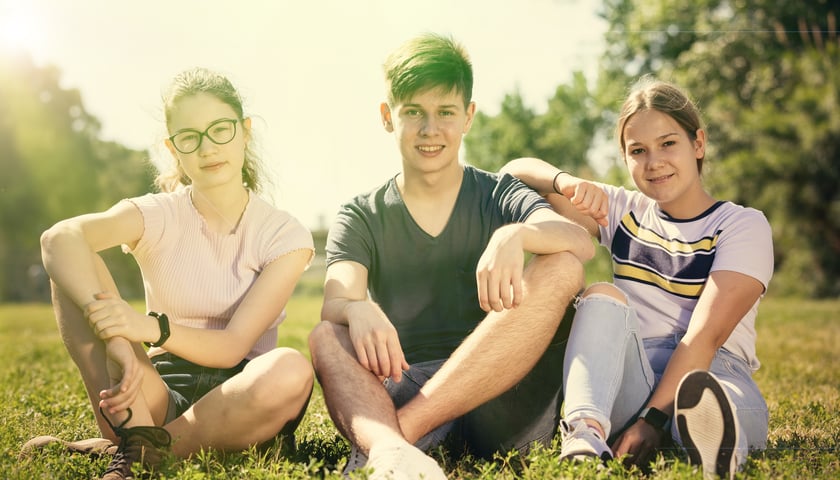 Trzy młode osoby siedzą na trawie (zdjęcie ilustracyjne)