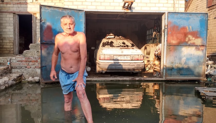Wasilij z Chersonia stoi na podwórku swojego domu zalanego przez Dniepr. W tle w garażu jego samochód, który po powodzi nadaje się tylko na złom
