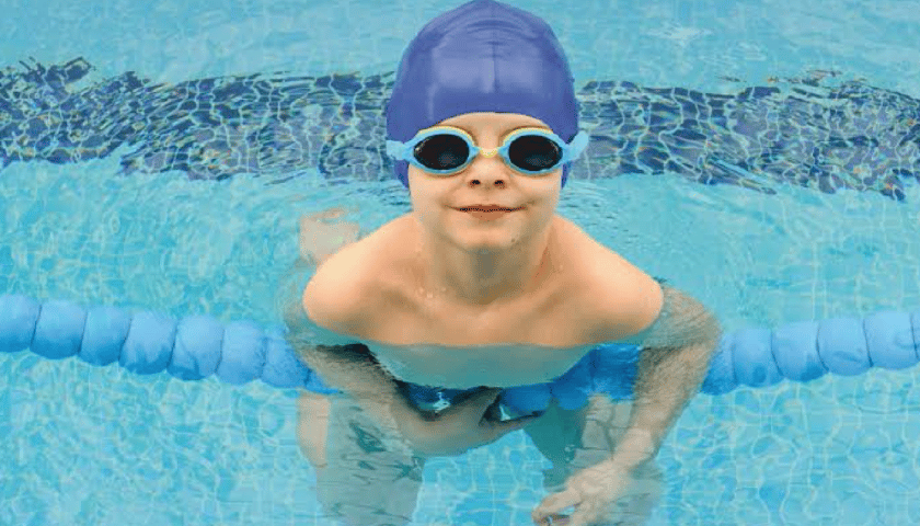 Kilkuletni chłopiec w czepku i okularach do pływania podczas zajęć na basenie. Zdjęcie ilustracyjne