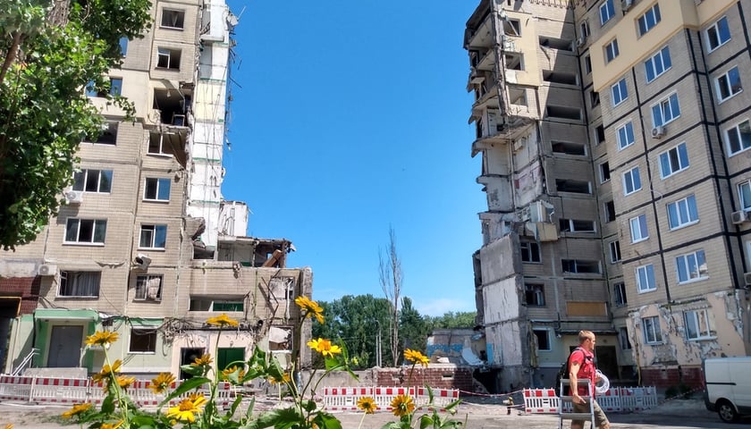 Dnipro, miasto w Ukrainie. Po prawej i lewej bloki, w środku ogromna wyrwa powstała na skutek uderzenia rosyjskiej rakiety. Przed blokami idzie mężczyzna z niewielką drabiną w dłoni  