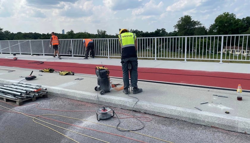 Robotnik w żółtej kamizelce i kasku, z młotem pneumatycznym, pracuje na moście Olimpijskim (zdjęcie z pierwszych dni lipca)