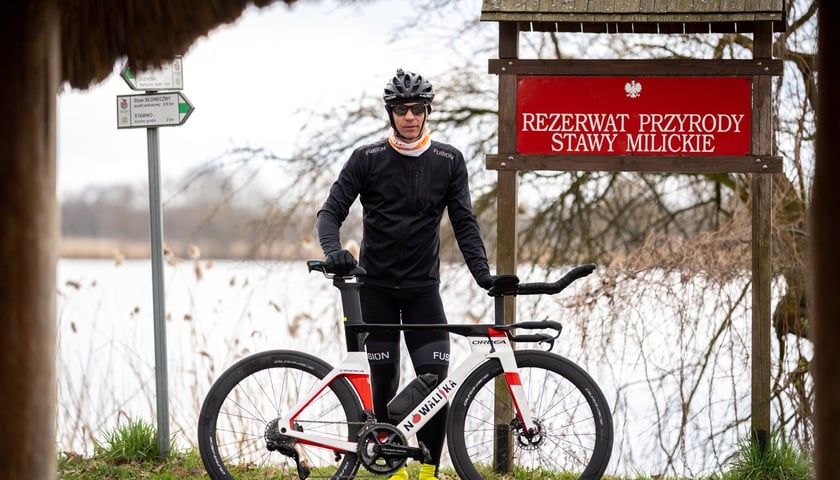 Adrian Kostera z rowerem obok czerwonej tablicy z napisem REZERWAT PRZYRODY STAWY MILICKIE