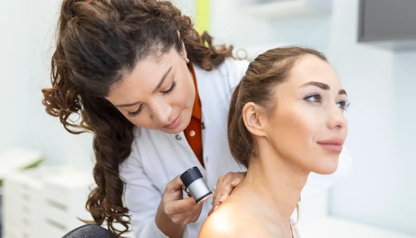 Badanie dermatologiczne. Na zdjęciu kobieta w stroju lekarskim obserwuje przez wizjer skórę młodej kobiety. Zdjęcie ilustracyjne