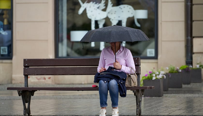Kobieta pod parasolem, siedzi na ławce w rynku