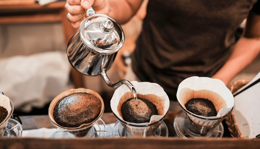 Na zdjęciu barista przelewa kawę przez specjalny filtr do filiżanek (przelewowa metoda parzenia kawy). Sprawdź kawowe ciekawostki!
