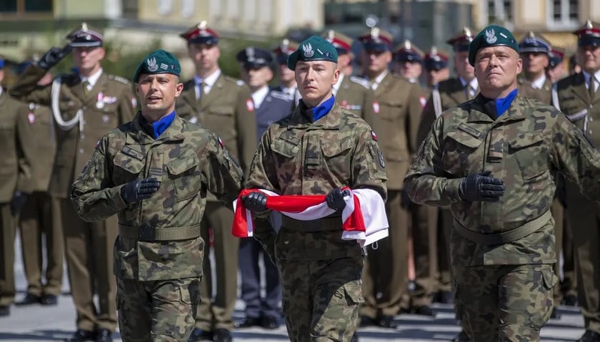 Żołnierze w mundurach podczas parady niosą flagę biało-czerwoną, zdjęcie ilustracyjne