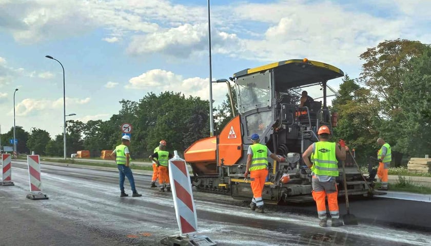 Na ul. Kosmonautów trwa układanie asfaltu. Na zdjęciu są pracownicy oraz specjalna maszyna.