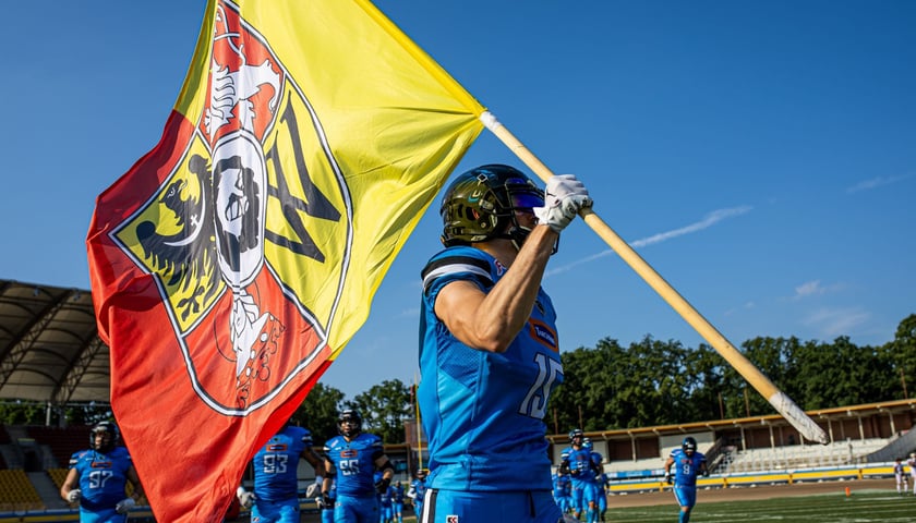 Zawodnik Panthers Wrocław na boisku z flagą Wrocławia. 