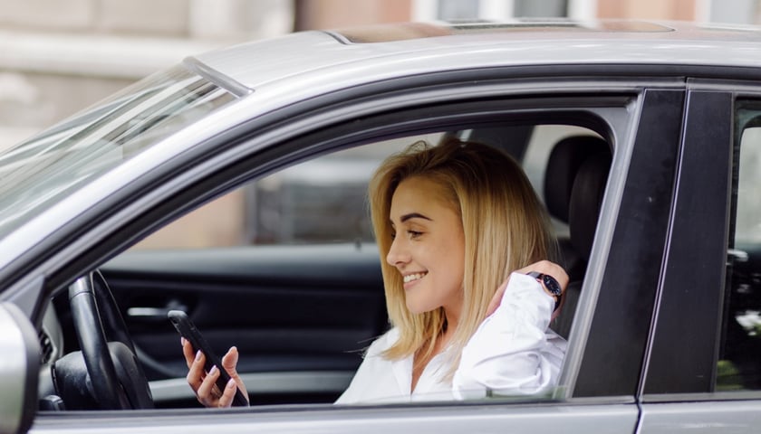 Płacenie za parkowanie przez smartfona jest wygodne. Na zdjęciu kobieta w samochodzie trzymająca w ręku telefon.