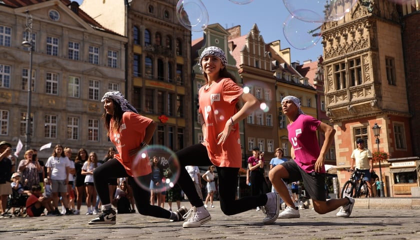 Dwie dziewczyny i chłopak klęczą na jednym kolanie, tańcząc tradycyjny taniec o nazwie debke