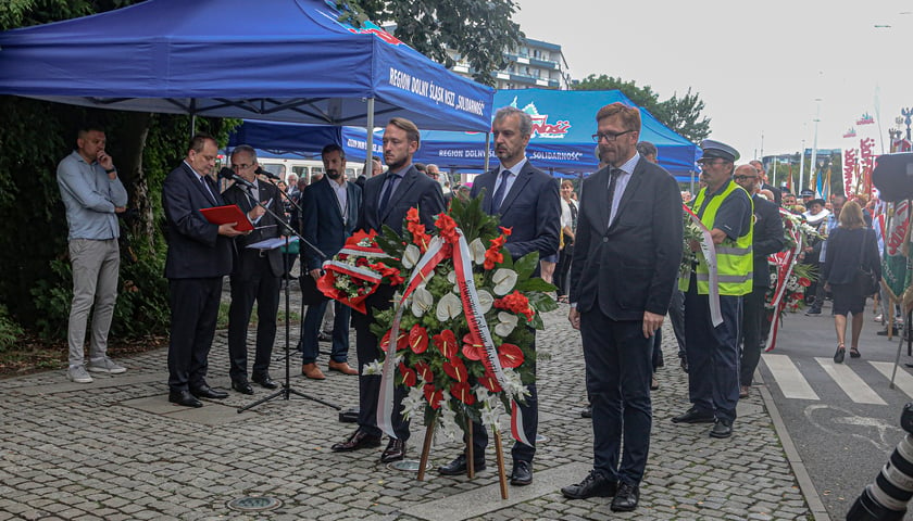 Obchody 43. rocznicy powstania NSZZ „Solidarność”. Mężczyźni składają kwiaty pod tablicą Solidarności