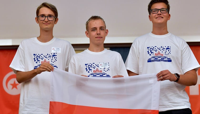 Trzech chłopców, którzy przed sobą trzymają rozpostartą flagę Polki