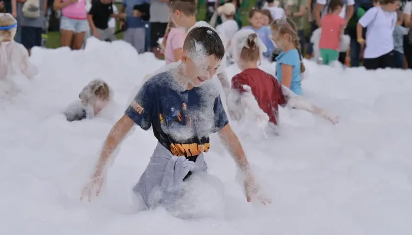 Dzieci bawiące się w pianie wypuszczonej przez strażaków. Była to jedna z wielu atrakcji podczas Festiwalu Pierwszej Pomocy.  