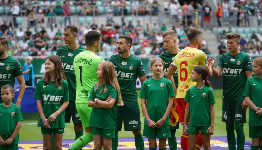 Zawodnicy Śląska Wrocław w zielonych strojach na stadionie przed meczem z Jagiellonią. Przed nimi dzieci w zielonych strojach.