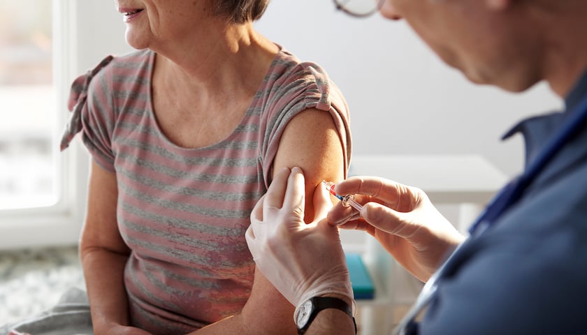 Starsza kobieta ubrana w bluzkę z krótkim rękawkiem przyjmuje szczepionkę