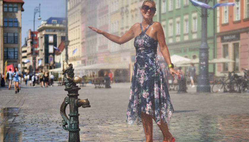 Kobieta w letniej sukience stojąca przy wodnej kurtynie we wrocławskim Rynku i schładzająca się w upalny dzień, zdjęcie ilustracyjne.