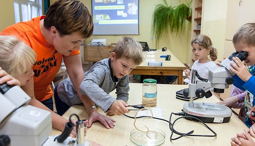 Dzieci w wieku wczesnoszkolnym stoją przy stole z mikroskopami 