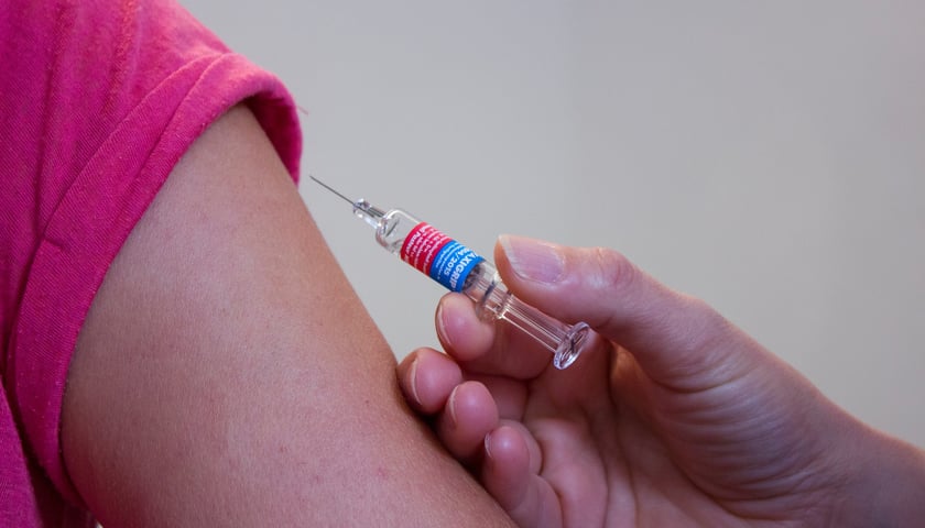 Strzykawka ze szczepionką obok ręki dziecka/zdjęcie ilustracyjne