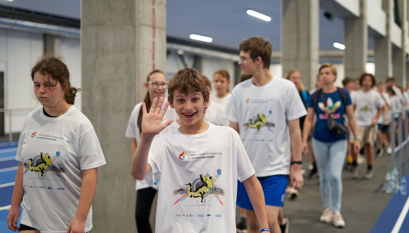 Uśmiechnięty chłopak unosi dłoń, idąc po bieżni w hali sportowej Ślęzy na Kłokoczycach