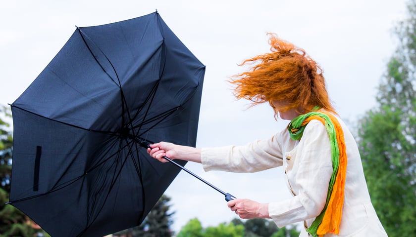 Front atmosferyczny przyniesie zmianę pogody. Na zdjęciu rudowłosa kobieta trzymająca parasol odwrócony przez wiatr