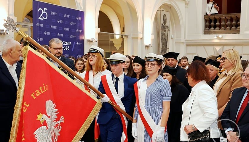 Studenci wnoszą sztandar czerwony z białym orłem 