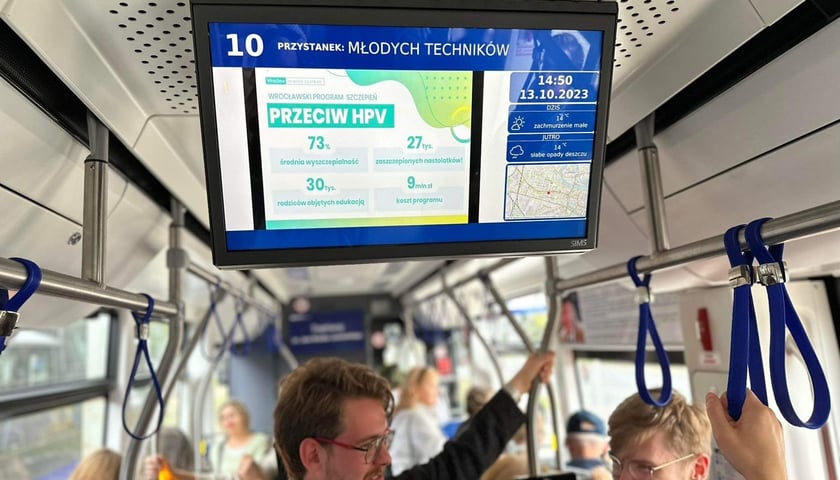 Pasażerowie w tramwaju 10, na wyświetlaczu: grafika promująca szczepienia przeciwko HPV