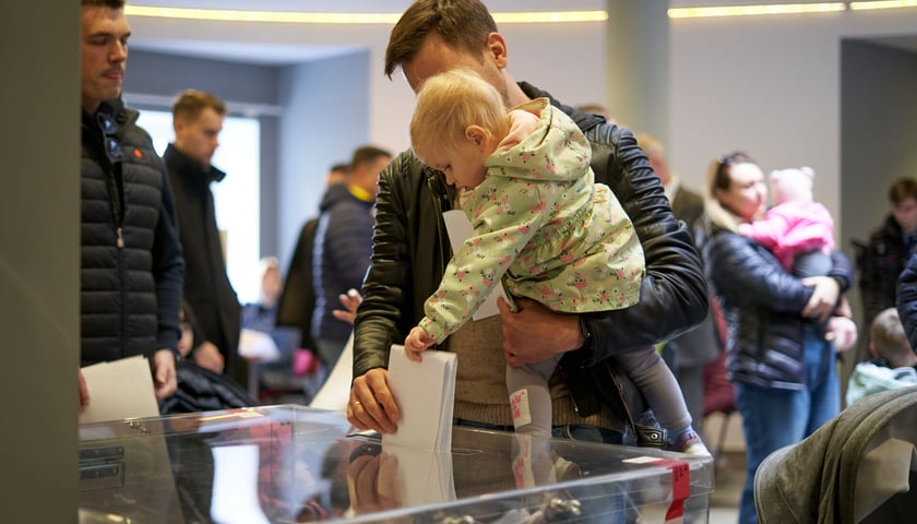 Mężczyzna z dzieckiem na ręku wrzucają głos do urny, wybory 2023 we Wrocławiu