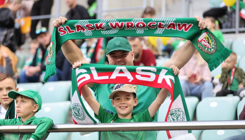 Kibice Śląska Wrocław na meczu z Legią z szalikami klubu. Na pierwszym planie chłopiec w zielonej koszulce