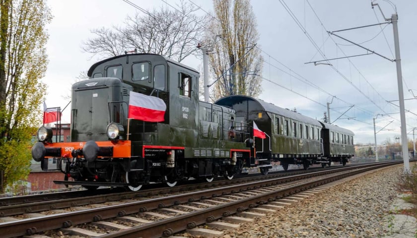 Pociąg retro. Na zdjęciu stara lokomotywa i wagony. Na pociągu zawieszone są biało - czerwone flagi