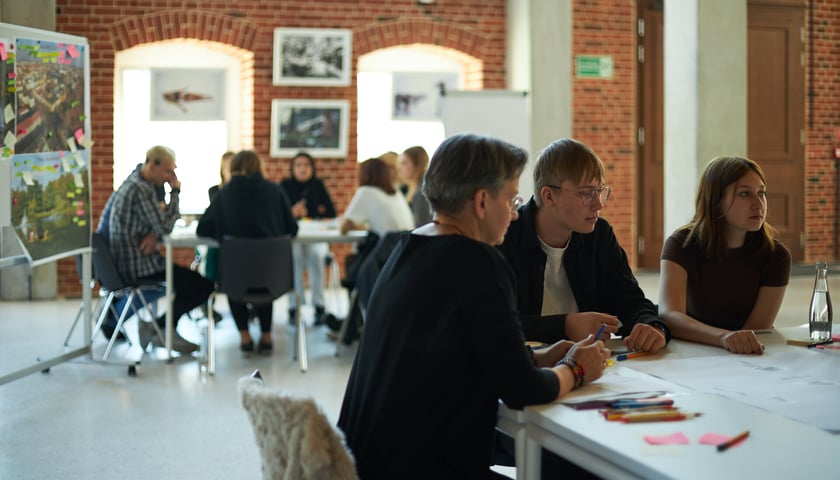 Uczestnicy warsztatów siedzący przy stolikach. Zdjęcie ilustracyjne wykonane w 2022 roku podczas badań fokusowych z udziałem młodzieży w Concordia Design.