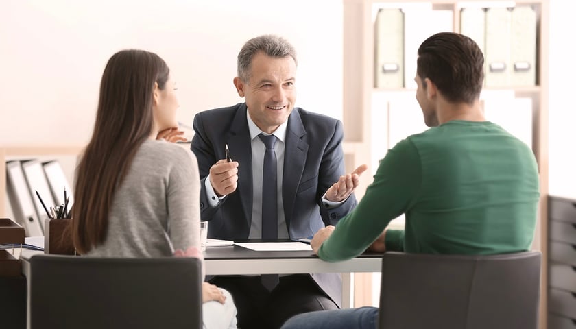 Na zdjęciu elegancki mężczyzna rozmawia z młodymi ludźmi siedząc przy stoliku