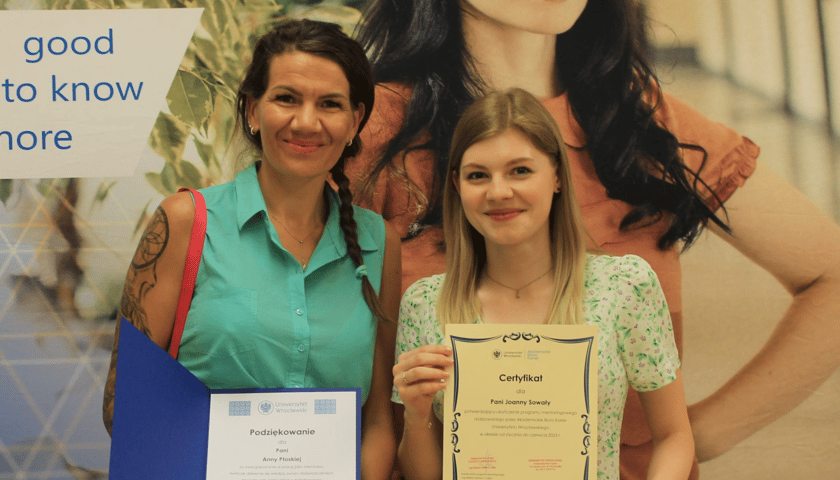 Dwie kobiety na tle baneru Uniwersytetu Wrocławskiego: mentorka i mentee, uczestniczki Programu Mentoringowego 2022/2023 