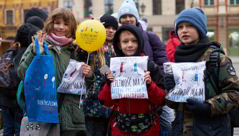 Na zdjęciu uśmiechnięte dzieci z gadżetami (płócienna torba, zapakowane koszulki, balonik) związanymi z Dniem Życzliwości