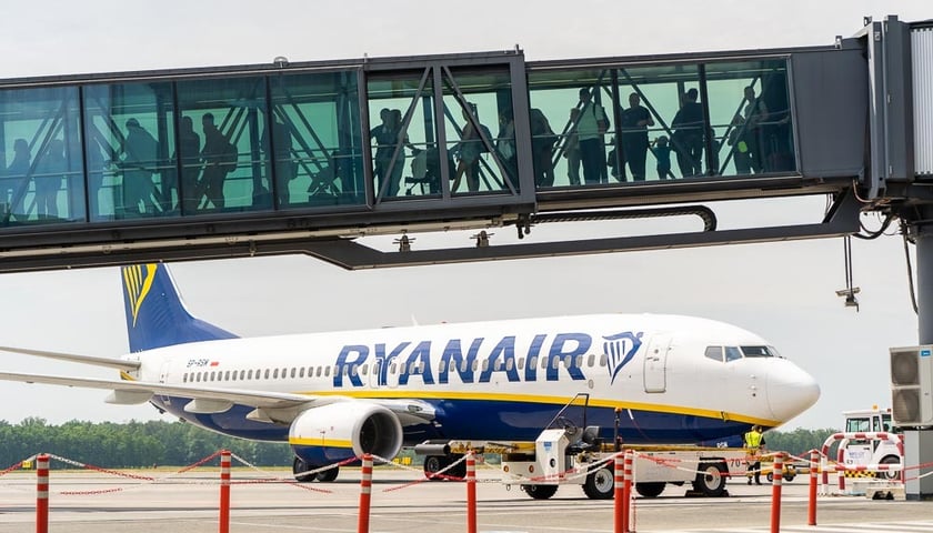 Samolot Ryanair stojący na płycie lotniska, w tunelu do samolotu zmierzają pasażerowie