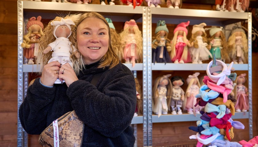 Uśmiechnięta kobieta z lalką w ręku na jednym ze stoisk Jarmarku Bożonarodzeniowego
