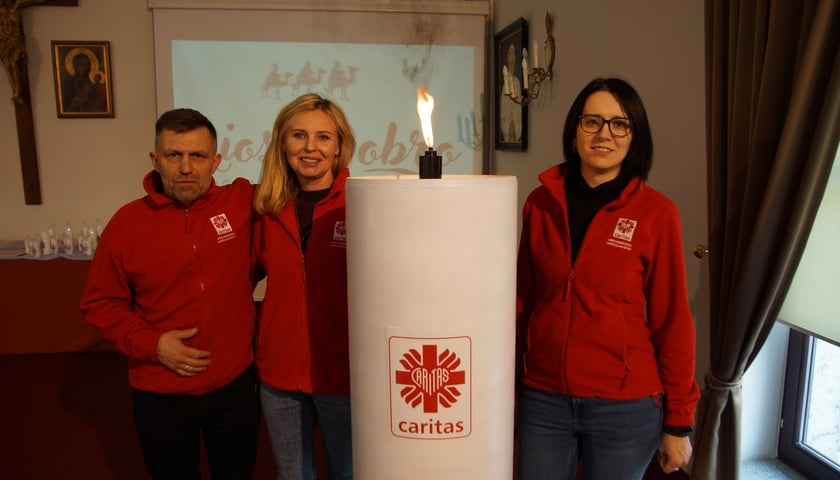 Wolontariusze Caritas obok wielkiej, jubileuszowej świecy wigilijnej