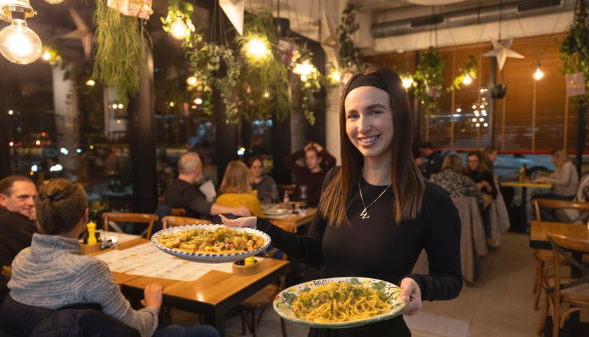 Uśmiechnięta kelnerka restauracji Ragu z dwoma talerzami z makaronami w dłoniach