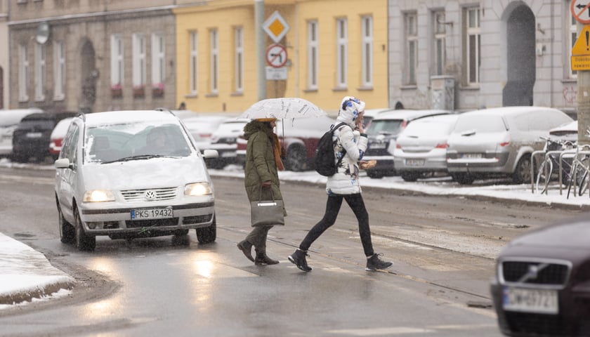 Ludzie idący po ulicy, jedna z osób trzyma parasolkę