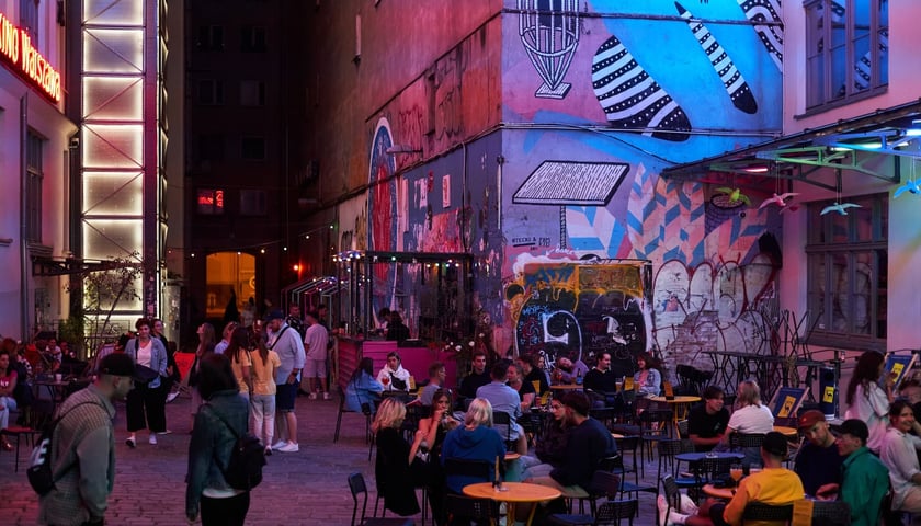 Podwórko przy ulicy Ruskiej na Starym Mieście wieczorową porą. Ludzie przy stolikach restauracyjnych, barwne poświaty od neonów. Zdjęcie ilustracyjne.