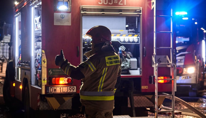 Rozświetlony wóz strażacki, na pierwszym planie strażak