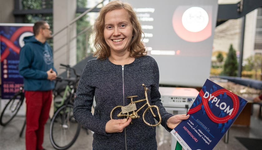 Kobieta z dyplomem i statuetką w kształcie roweru; AleksandraSZ zwyciężczyni rywalizacji "W kółko kręcę" edycja jesień 2023 