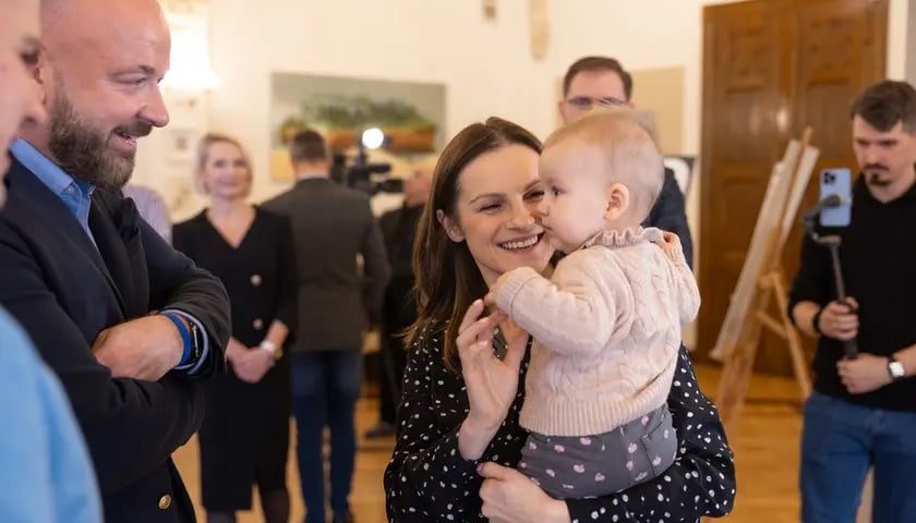 Prezydent Wrocławia Jacek Sutryk (po lewej) podczas konferencji w sprawie zmian w miejskim programie in vitro (15 grudnia 2023 r.). Obok Marta Bułka 8-miesięczną Łucją