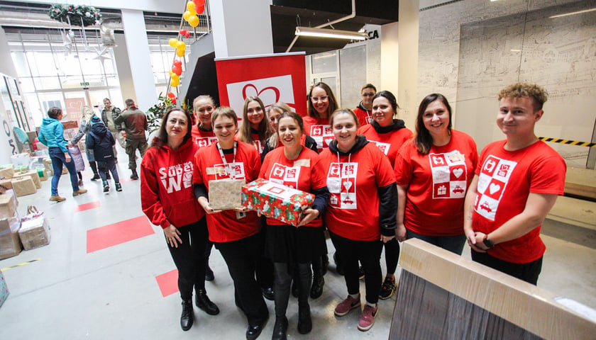 Grupa wolontariuszy Szlachetnej Paczki w czerwonych koszulkach, z paczkami w rękach, w magazynie we Wrocławiu
