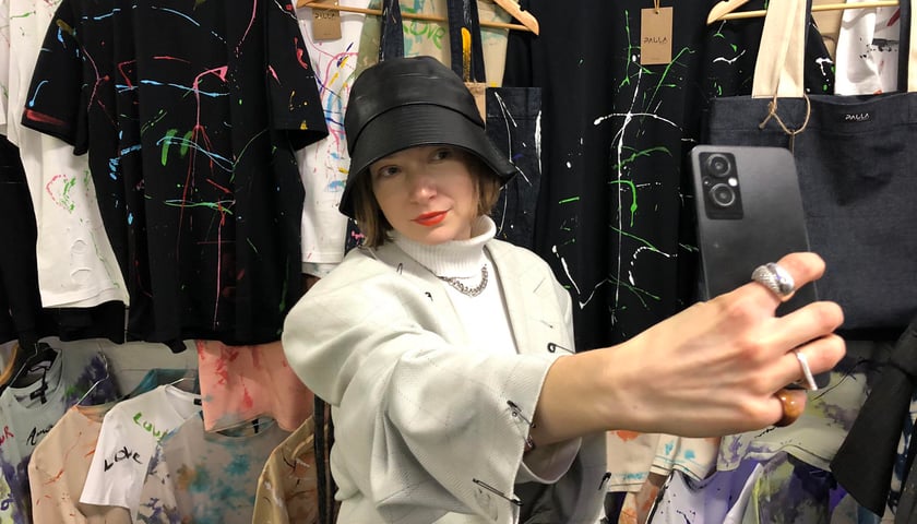 Młoda kobieta w kapeluszu z telefonem w ręce. Stoisko na Alternatywnym Jarmarku Świątecznym