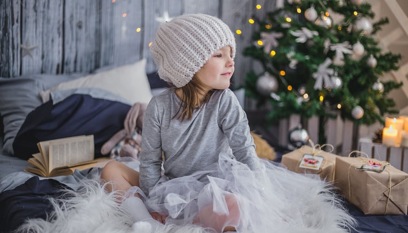 Dziecko z prezentami - ilustracyjne zdjęcie, na którym widać klimat świąt Bożego Narodzenia. Dziecko-dziewczynka siedzi, a w tle jest choinka