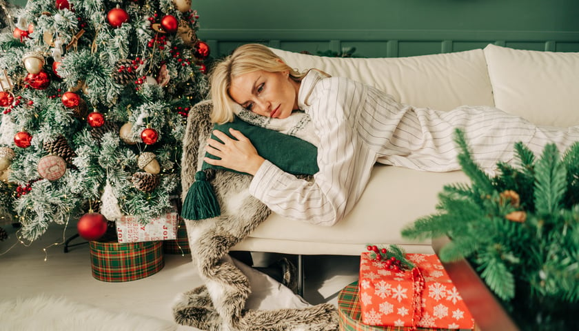Młoda kobieta leży smutna na kanapie w świątecznie przystrojonym pokoju 