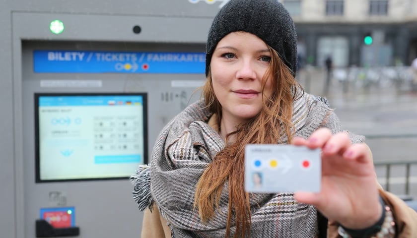 Kobieta w czapce pokazuje swoją kartę miejską. Za nią automat do kupowania Urbancard (zdjęcie ilustracyjne)