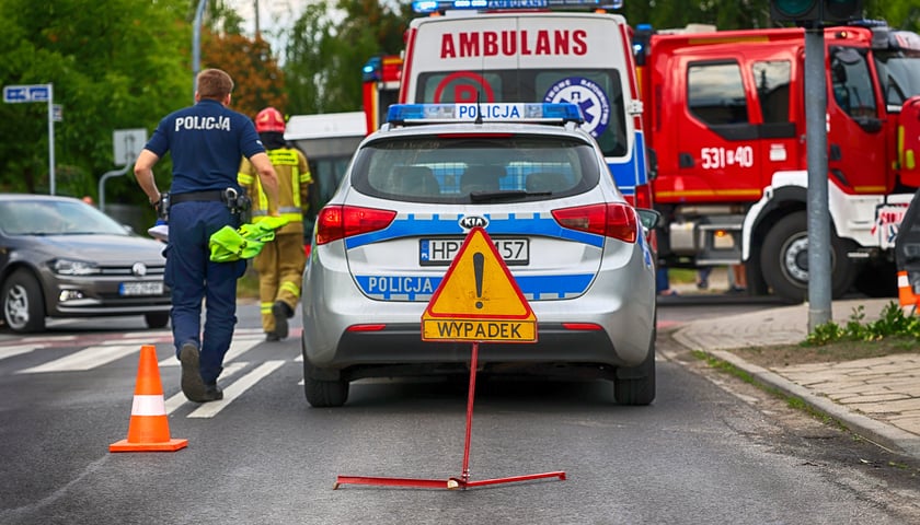 Znak informujący o wypadku, na dalszym planie stoi radiowóz i ambulans / zdjęcie ilustracyjne 