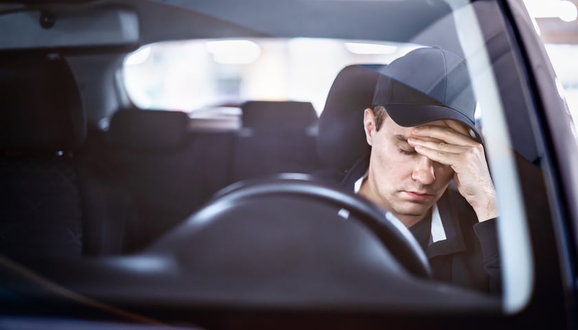 Na zdjęciu smutny młodych mężczyzna za kierownicą auta. Zdjęcie ilustracyjne