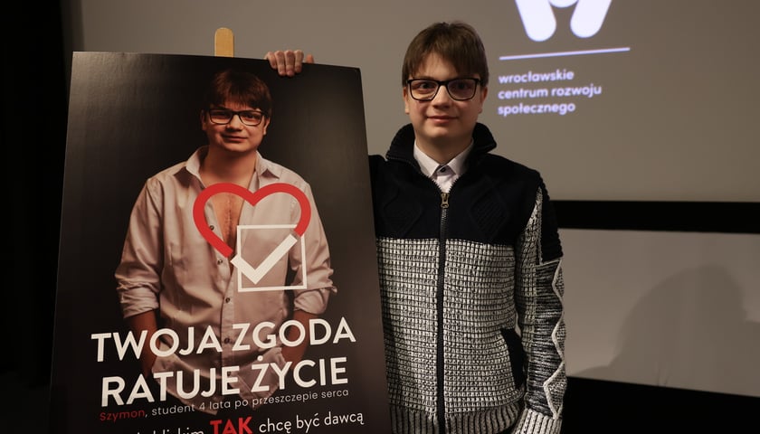 Szymon Konieczny, twarz kampanii „Zgoda to dar życia. Tak, chcę być dawcą”, przed plakatem z napisem „Twoja zgoda ratuje życie"